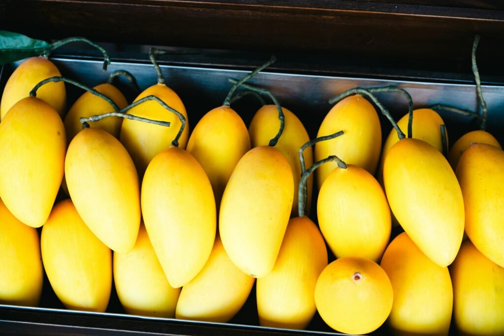Bright yellow mangoes with twigs, neatly arranged in a tray, showcasing freshness and vibrant color.