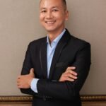Confident businessman in suit arms crossed against elegant interior wall.