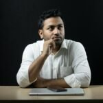 Thoughtful businessman seated at a desk with a laptop and phone, deep in reflection.